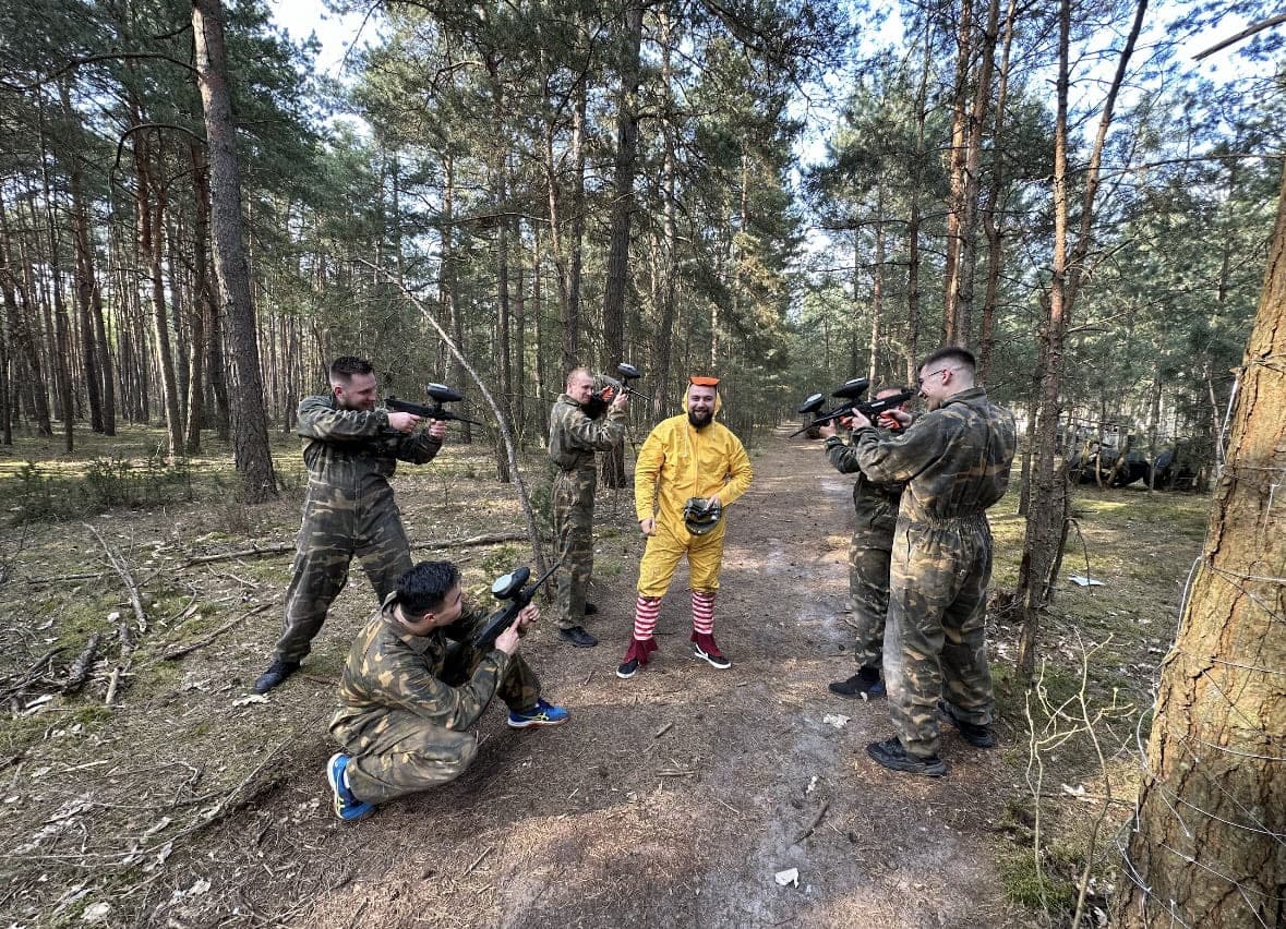 Gracze paintball otaczają uczestnika w żółtym stroju na leśnej ścieżce, Siedlisko Rawka Nowy Kawęczyn