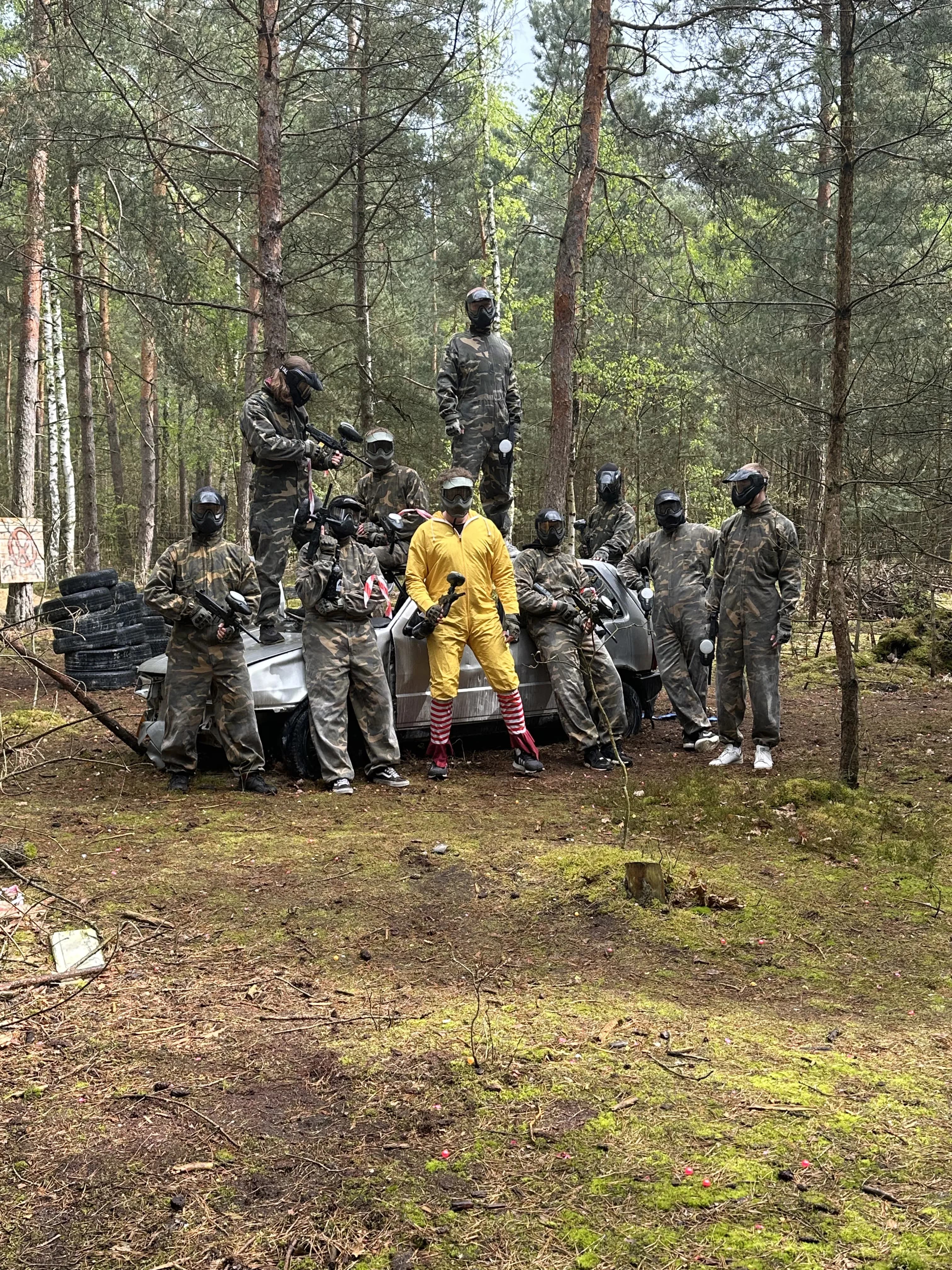 Gracze paintball otaczają uczestnika w żółtym stroju na leśnej ścieżce, Siedlisko Rawka Nowy Kawęczyn
